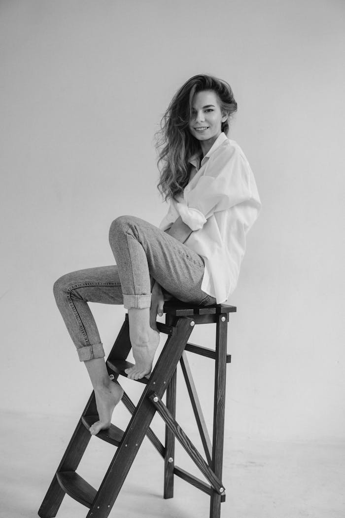 Elegant black and white portrait of a smiling woman posing on a ladder in a studio.