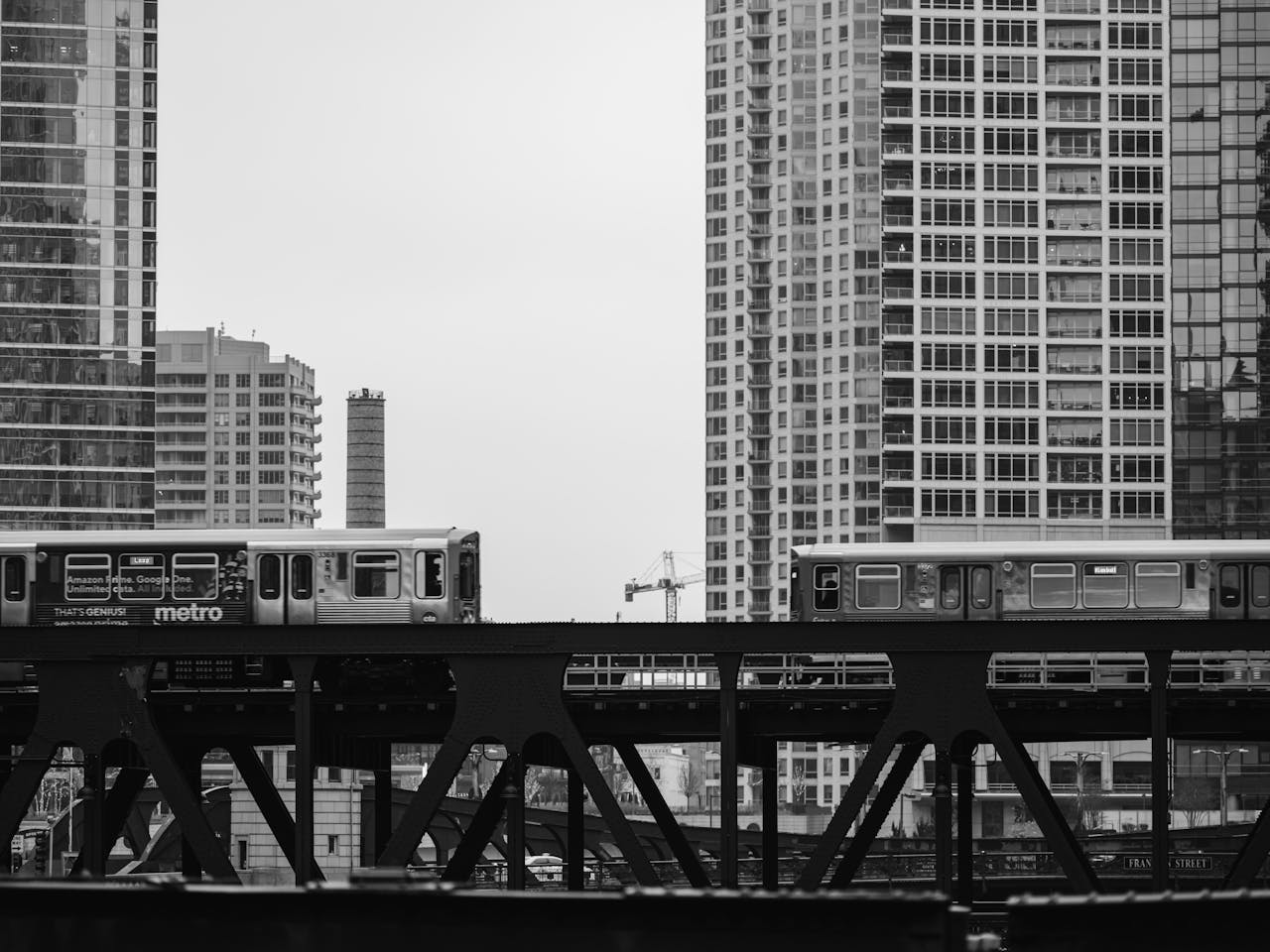 Monochrome image of a metro train traversing a cityscape with high-rise buildings.