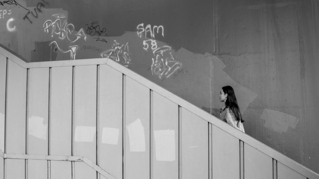 A woman walks up a staircase adorned with urban graffiti art in a minimalist black and white setting.