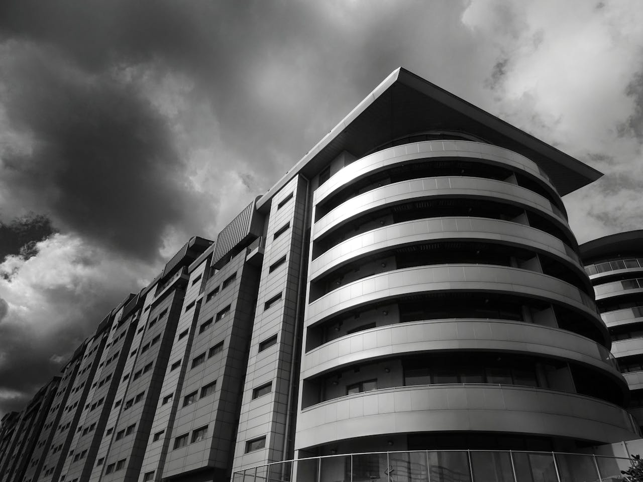 Dramatic black and white photo of a modern, futuristic building with glass and steel elements under a cloudy sky.